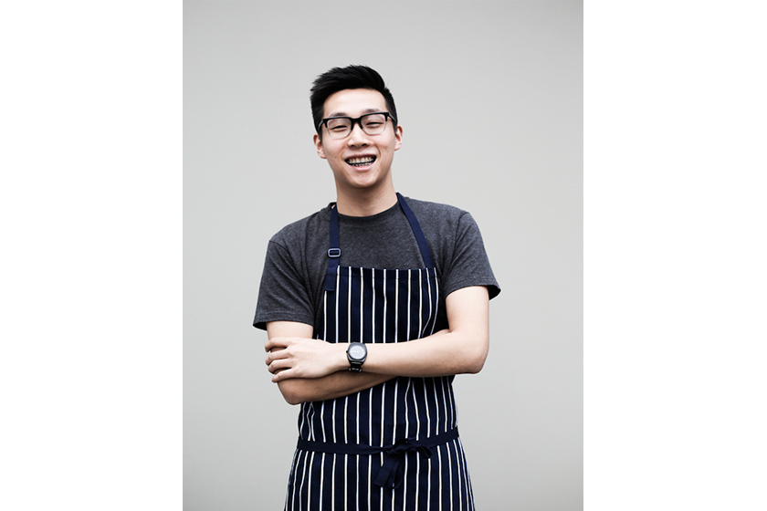 A young man with glasses wearing striped apron is smiling