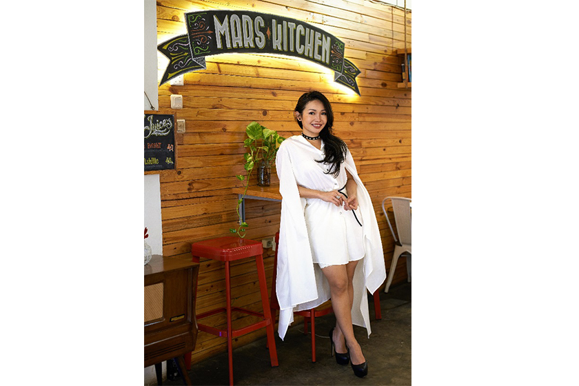 A long haired women with white dress shirt is standing in front of Mars Kitchen logo