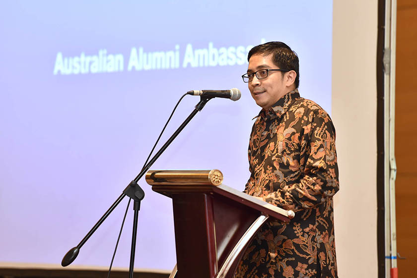 A man with glasses wearing formal batik shirt giving speech on the podium