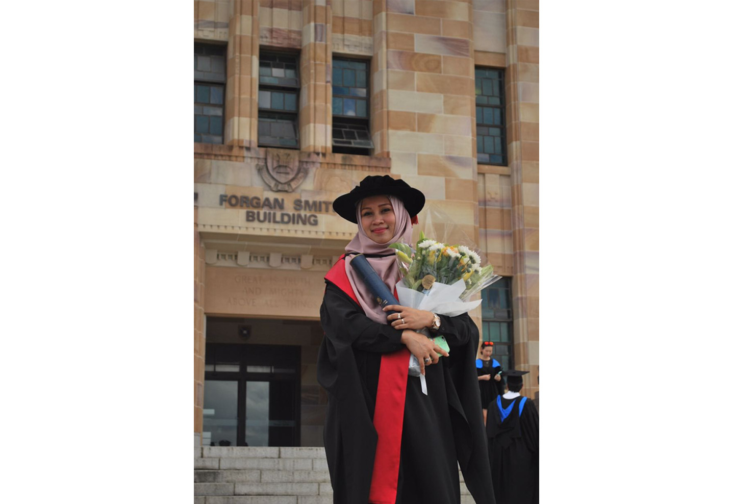 A woman with hijab with graduation attire holding a flower bouquet